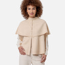 Mujer con capa de punto color crudo Surkana combinada con camisa blanca y pantalón en tonos claros.