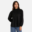Modelo con blusa negra Feeka de algodón 100% con cuello alto fruncido y silueta fluida.