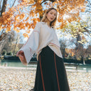 Mujer con jersey de punto fino crudo de PAN Producto Básico combinado con pantalón negro en un parque otoñal.